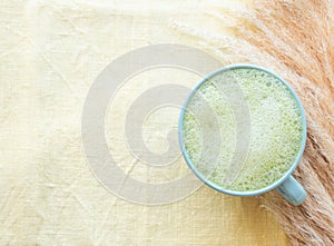 Matcha tea latte morning antioxidant hot drink in blue cup on yellow table cloth with pampas grass