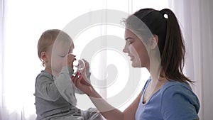 Maternal care, happy laughing toddler boy drinking pure mineral water from glass from smiling mother hands and rejoices