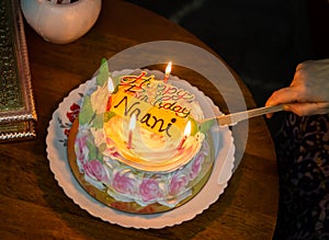 maternal grandmother cutting birthday cake decorated with lighted candles at coffee table