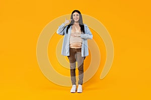 Maternal health and beauty. Young pregnant woman showing and pointing at perfect teeth, standing on yellow background