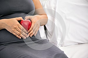 Maternal Love: Asian Pregnant Woman with a Red Heart Symbol, Sitting on Bed
