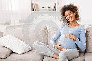 Happy pregnant woman sitting on sofa and caressing her belly