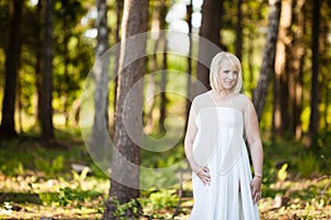 Maternity photo shoot in nature. Pregnant woman in her 30`s in white long sheer dress.