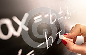 Math teacher writing function, equation or calculation on blackboard in school classroom.