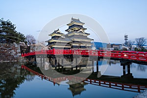 Matsumoto castle water reflection with sakura tree around and red bridge in front against blue clear sky background, castle`s shad