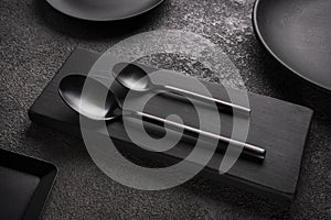 matte black spoons and surrounded by plates and utensils on a dark concrete. concept for a restaurant or cafe, coffee