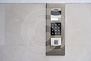 Matte metal intercom call panel with white digital buttons and fingerprint scanner on limestone wall of luxury