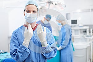 A matter of life and death. Portrait of a female surgeon wearing gloves ready to perform surgery with her colleagues.