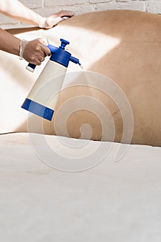 Mattress cleaning. Spraying detergent on mattress for dry cleaning. Professional cleaner in gloves is pouring detergent