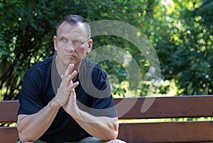 Mature 50-year-old handsome courageous man with a pensive look sits on a park bench