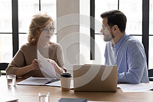 Mature 60s female worker discussing marketing sales report with mentor.