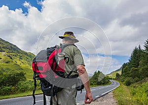 Mature active hiker with backpack walking away on the road. Euro