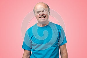 Mature adult in blue t-shirt having a doubt with disgust on face standing on pink background.