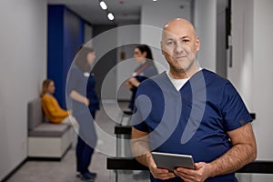 Mature adult man doctor in uniform with digital tablet in clinic corridor