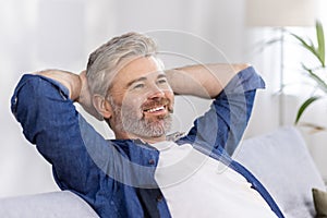 Mature adult man at home close up with hands behind head sitting on couch and thinking dreaming about future plans, gray