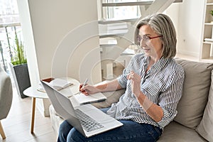 Mature adult old professional woman watching training webinar on laptop at home.