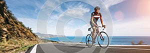 Mature Adult on a racing bike climbing the hill at mediterranean sea landscape coastal road