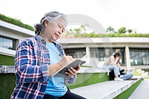 Mature adult student sitting in front off College building and reading school books after attending a university class, Adult