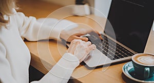 Mature adult woman hands, sitting in cafe with coffee mug and working online on laptop. Businesswoman typing on notebook