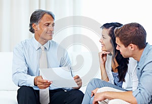 Mature advisor explaining financial plan to young couple. Mature advisor explaining financial plan to young couple at