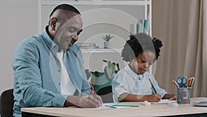 Mature african american father with little kid girl sitting in room at desk draws colored pencils dad and daughter play