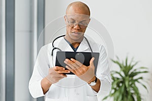 Mature african doctor using digital tablet in corridor . Portrait of confident male doctor using tablet computer in
