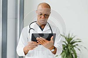 Mature african doctor using digital tablet in corridor . Portrait of confident male doctor using tablet computer in