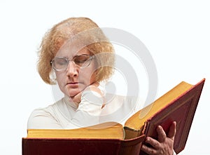 Mature age woman with glasses sits while reading old red paperback book Bible