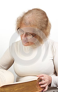 Mature age woman with glasses sits while reading old red paperback book Bible