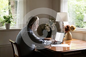 Mature aged man writer typing on laptop working on book