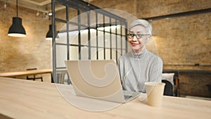 Mature asian business woman wears glasses using laptop computer sit at workplace desk