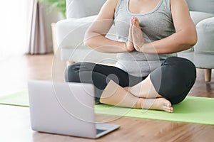 Mature Asian chubby fat woman sitting on the floor in living room practice online yoga lesson with the computer. female having