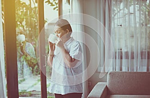 Mature Asian woman drinking hot coffee near window in the morning at home,Happy and smiling,Positive thinking