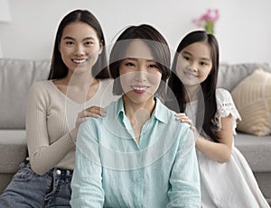 Mature Asian woman with her adult daughter and cute granddaughter posing at home, selective focus
