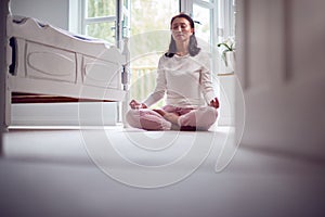 Mature Asian Woman In Pyjamas Sitting On Bedroom Floor Meditating In Yoga Pose