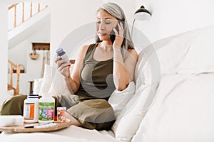 Mature asian woman taking her medication while talking on cellphone