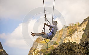 Mature attractive and happy woman on with grey hair enjoying amazing rock cliff view from swing feeling young and free swinging