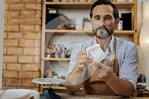 Mature bearded ceramist looking at his handiwork