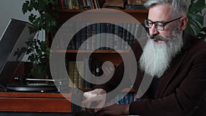 Mature bearded man choosing record and puts it in turntable, listens to music, selective focus