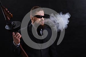 Mature bearded man in sunglasses dressed in suit with tommy gun