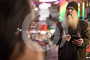Mature bearded tourist man asking directions from young woman in Chinatown at night