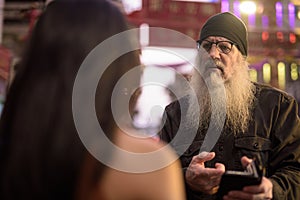 Mature bearded tourist man asking directions from young woman in Chinatown at night