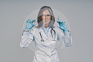 Mature beautiful female doctor in face shield holding syringe