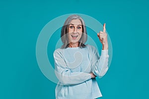 Mature beautiful woman looking at camera and smiling while standing against blue background