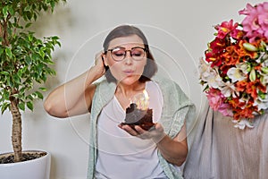 Mature beautiful woman with small birthday cake with burning candles