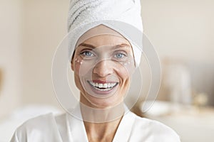 Mature beauty concept. Charming happy caucasian woman with face cream under her eyes, smiling to camera at home