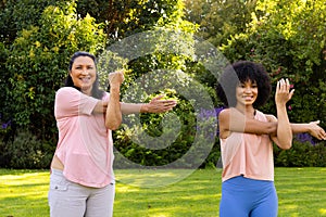 Mature biracial woman and young biracial woman exercising in garden at home photo