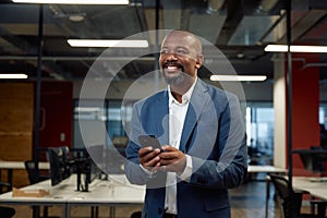 Mature black man in businesswear smiling while using mobile phone in office