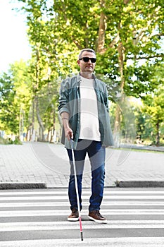 Mature blind person with white cane crossing street photo