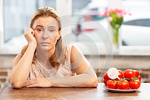 Mature blond-haired woman sitting at the table having food allergy